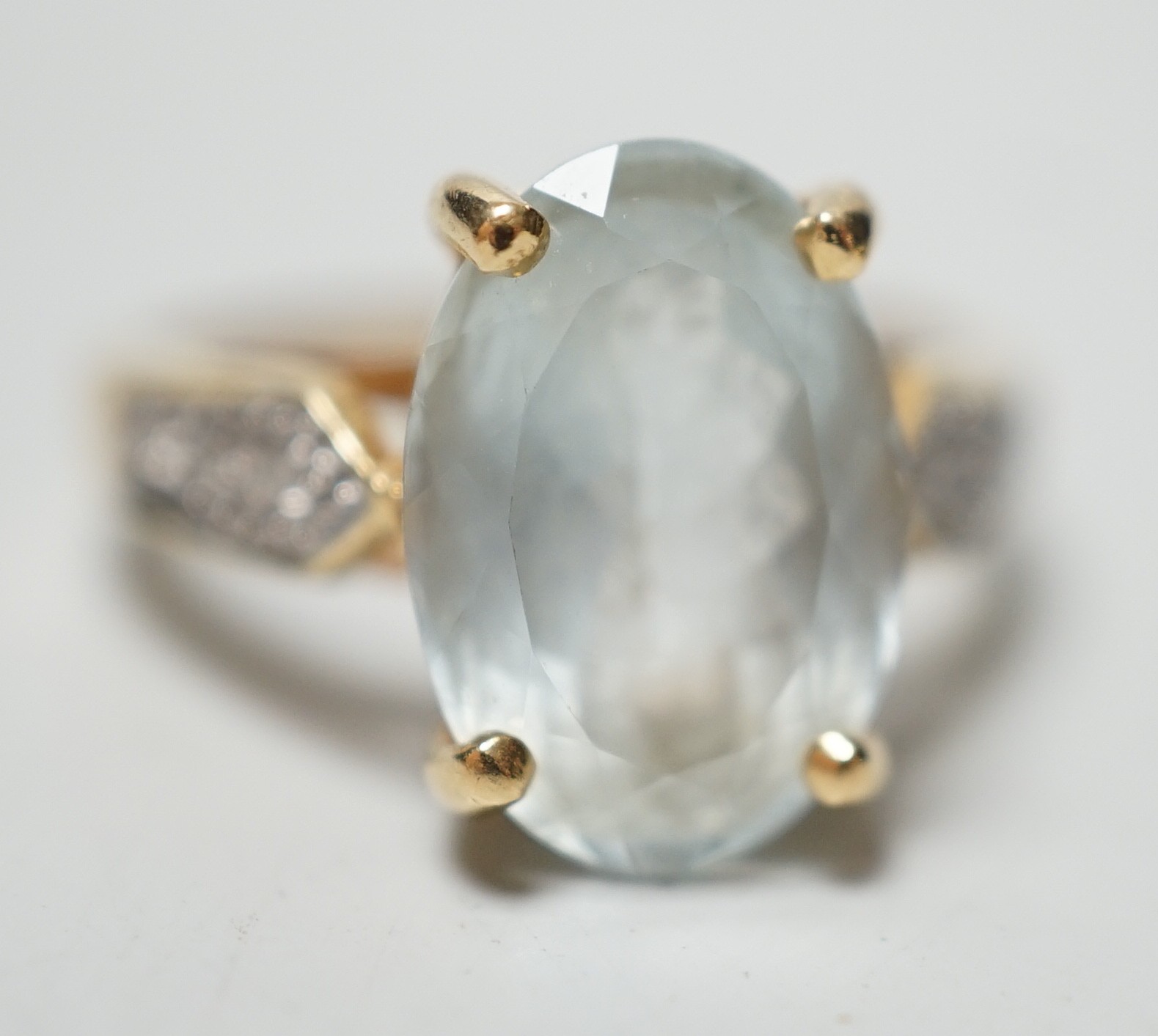 A modern 18ct gold and oval cut aquamarine set dress ring, with diamond chip set shoulders, size N, gross weight 5.5 grams.